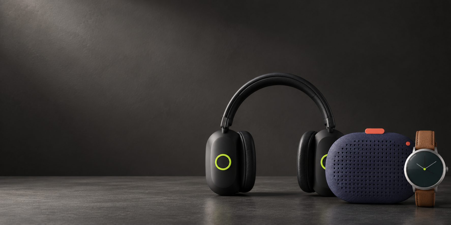 Headphones, a speaker and a watch on a dark table